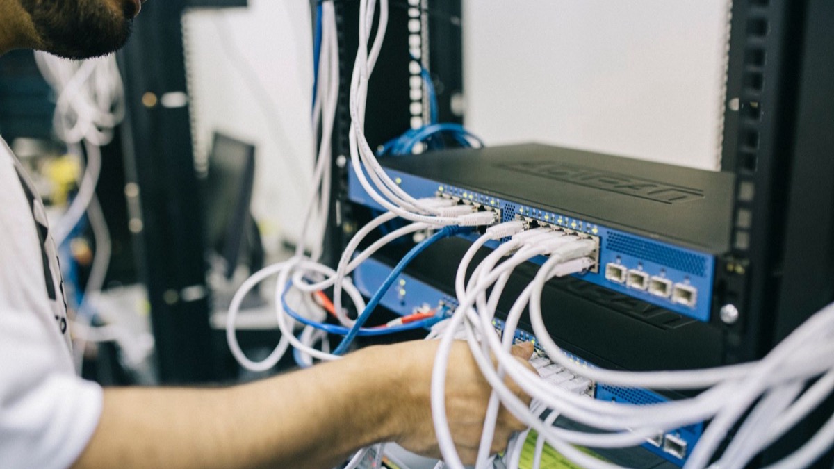 A technician plugging network cables into a switch in a server rack, illustrating self-hosting an open-weights model on-premise