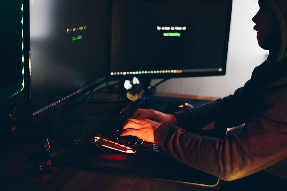 Hooded hacker typing on a keyboard in the dark