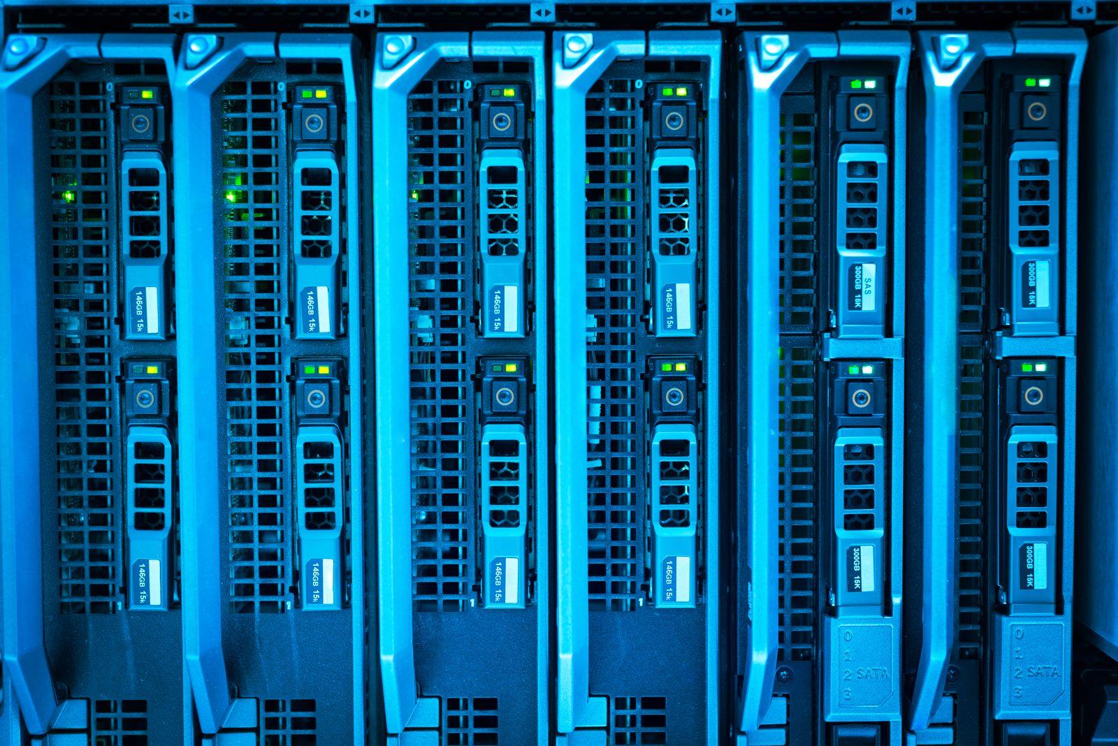 Head-on close-up of six blade server trays racked side by side in one chassis, with perforated front panels, metal release levers, green and yellow status LEDs and 146GB 15k and 300GB 15K drive labels, the whole frame bathed in cold blue light