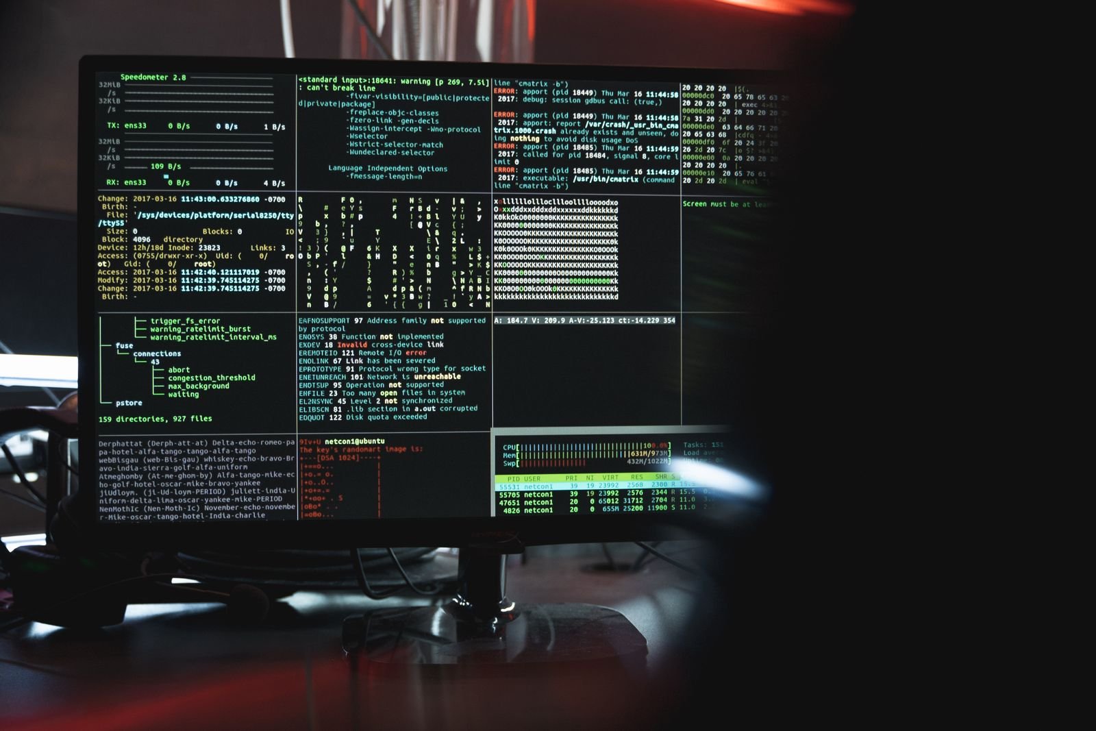 Screen in a dark room showing multiple terminal panes with system logs, error codes and CPU and memory stats
