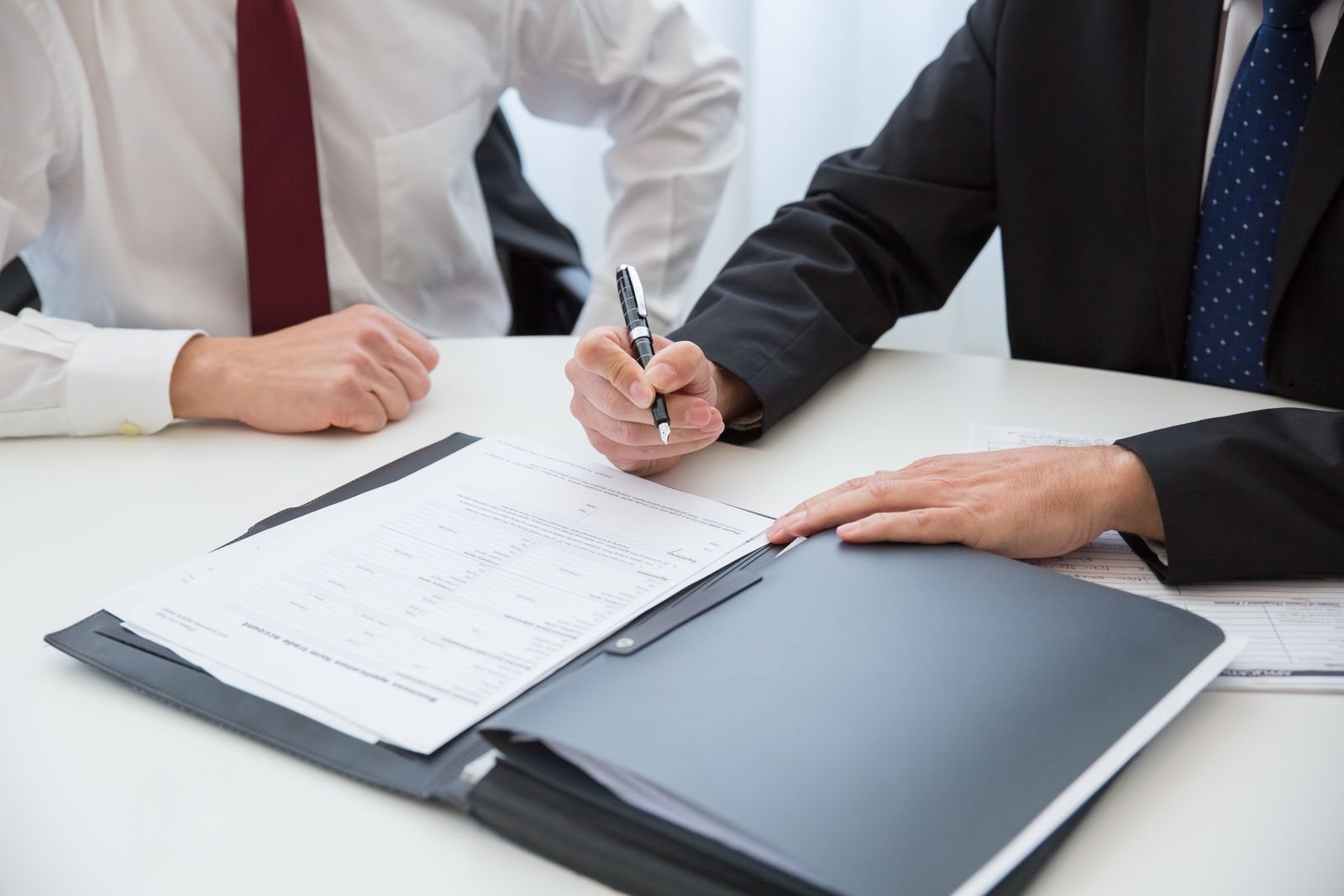 Two people in suits, one signing a document in a folder on a desk — illustrating the signing of an executive order